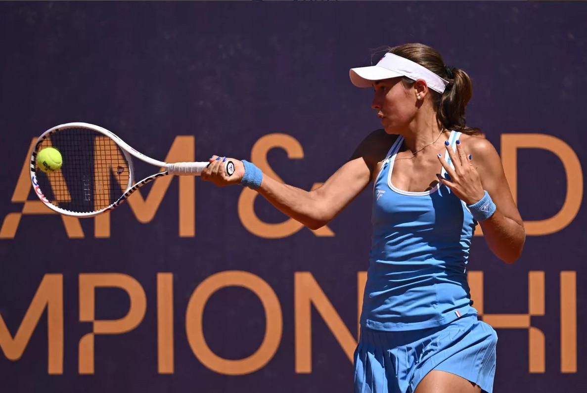 Joueuse de tennis en action, portant une robe bleue et casquette blanche, frappant la balle avec une raquette lors d’un match.