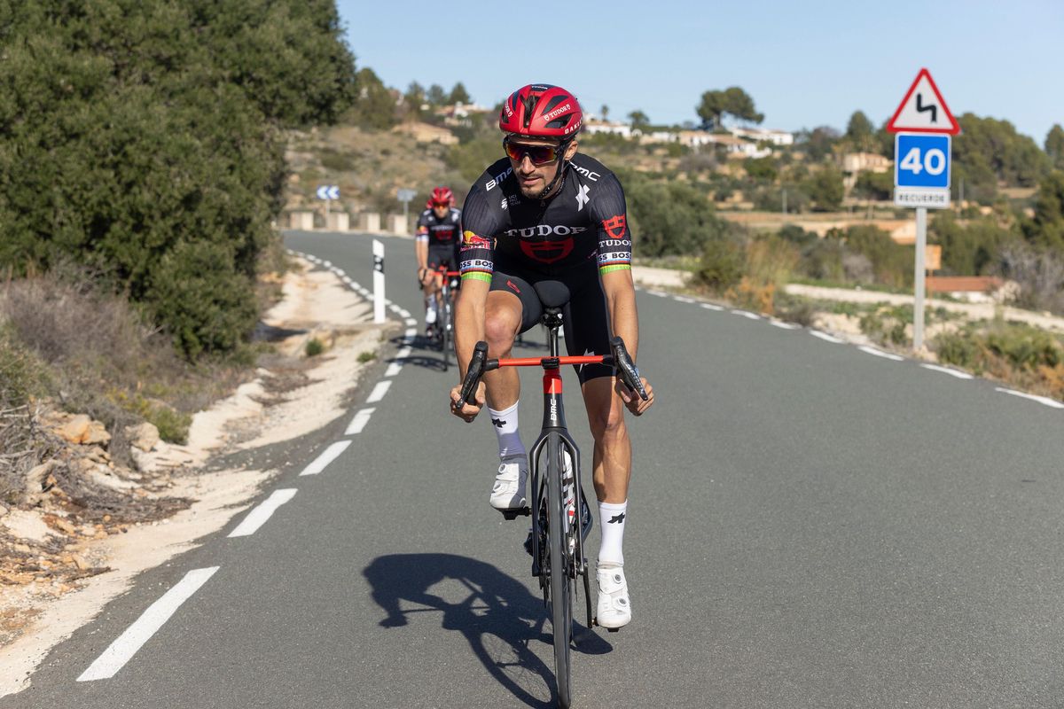 Cycliste sur une route de montagne, portant un maillot noir et un casque rouge, avec un panneau de limitation de vitesse à 40 km/h en arrière-plan.