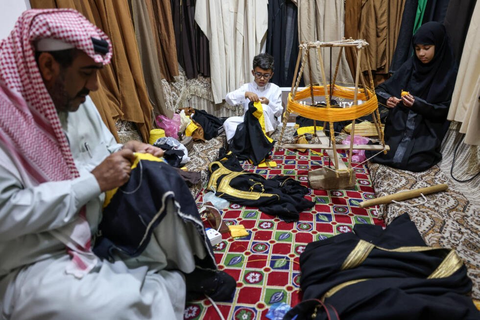 Le tailleur Habib Mohammed (g), son petit-fils Ghassan et sa petite-fille Fajr (d), travaillent sur la broderie de bishts, dans son atelier de l'oasis de Hofuf, en Arabie saoudite, le 16 février 2025