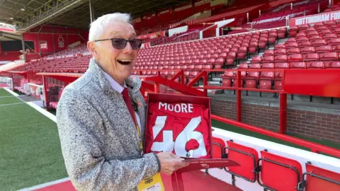 Alan Moore tenant un maillot signé en souvenir de ses 46 ans de service