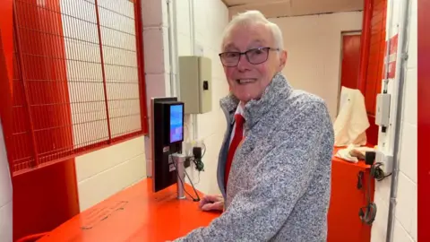 Alan Moore derrière un tourniquet, souriant